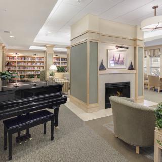 A cozy living room with a grand piano, fireplace, and extensive bookshelves.