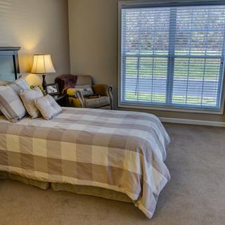 A cozy bedroom with a neatly made bed, a large window, and a comfortable chair.