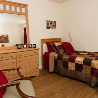 A cozy bedroom with a single bed, wooden dresser, and mirror.