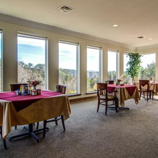 A well-lit dining area with tables and chairs, featuring large windows offering a scenic view.