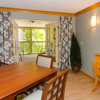 A cozy dining room with a wooden table, decorative curtains, and a view of the outdoors through large windows.