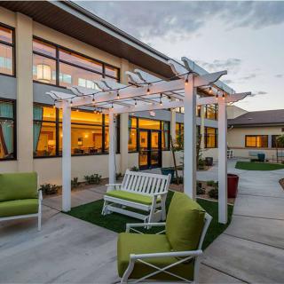 A cozy outdoor patio area with a pergola, swing, and green cushioned chairs at dusk.