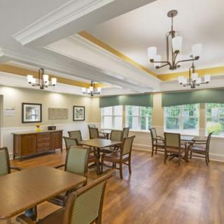 A well-lit dining room with wooden floors, tables and chairs, illuminated by chandeliers.