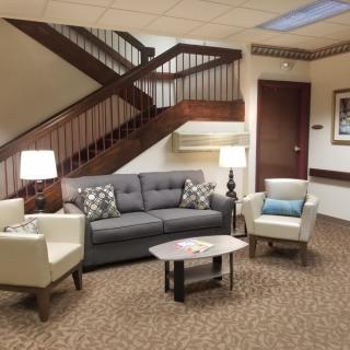 A comfortable lobby area featuring a sofa, two chairs, and a small coffee table with lamps under a staircase.