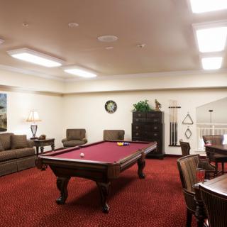 A cozy game room featuring a red pool table, comfortable seating, and warm lighting.
