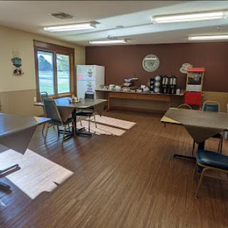A cozy indoor space with tables and chairs, featuring a kitchenette area for refreshments.