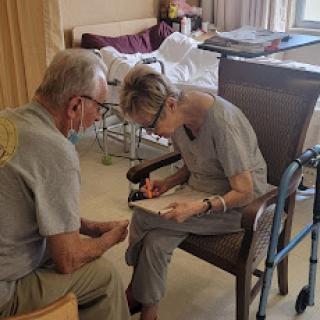 An elderly individual receives assistance from a caregiver while engaged in writing.
