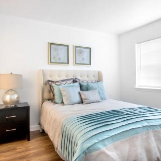 A modern bedroom with a neatly made bed, featuring decorative pillows and a matching comforter, accompanied by a nightstand and lamp.