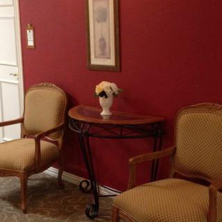 A cozy waiting area with two chairs, a table adorned with flowers, and a framed picture on a red wall.