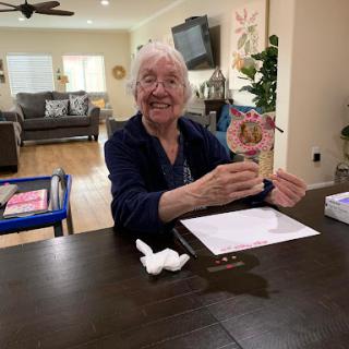 An elderly person joyfully showcasing their art project at a cozy home setting.