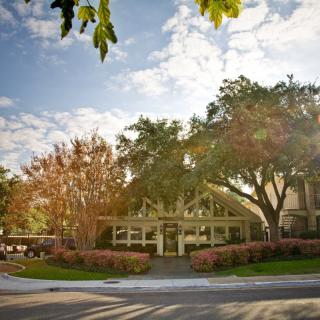A peaceful street view of a building surrounded by trees under a partly cloudy sky.