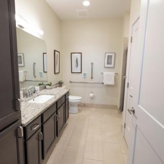 A modern bathroom with a sleek design featuring a large mirror, double sinks, and tiled flooring.
