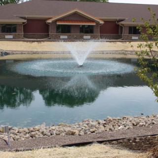 A peaceful pond with a central fountain in front of a building.