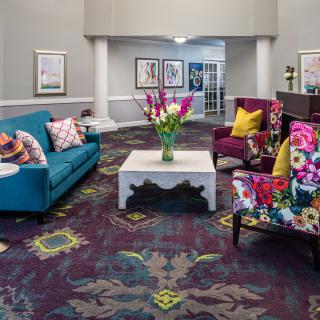 A vibrant and colorful hotel lobby featuring a mix of patterned armchairs, a teal sofa, and a white coffee table adorned with fresh flowers.