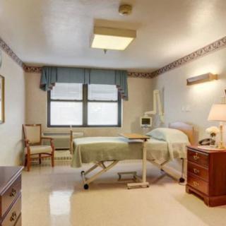 An empty hospital room with a single bed and medical equipment, featuring a window that allows natural light.