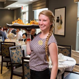 A smiling waitress carrying a tray of food in a restaurant.