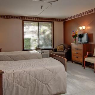 A cozy hotel room featuring two double beds, a TV cabinet, chairs, and soft lighting.