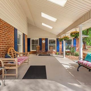 A welcoming covered porch with seating and skylights, featuring brick walls and vibrant plants.