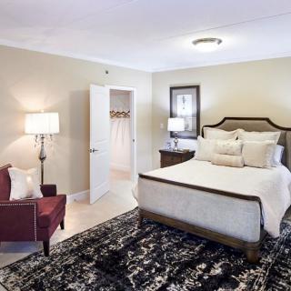 A cozy and elegantly decorated bedroom featuring a bed with plush pillows, a dark patterned rug, a red armchair, and soft lighting.