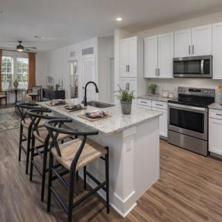 A modern kitchen with an island and bar stools, featuring stainless steel appliances and hardwood flooring.