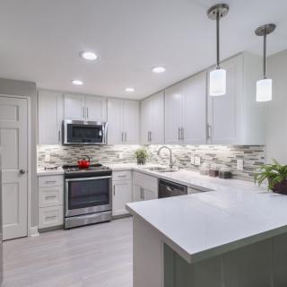 A modern kitchen with white cabinets, stainless steel appliances, and stylish lighting.