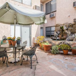 A cozy courtyard featuring a patio table with an umbrella, surrounded by potted plants and a decorative fountain.