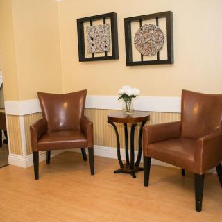 A cozy waiting area featuring two leather chairs, a small wooden table with a vase of flowers, and framed artwork on the wall.
