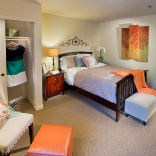 A cozy bedroom with warm decor, featuring a neatly made bed, a small closet, and a bedside lamp.