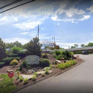 A scenic view of a landscaped area by the roadside, featuring a sign, trees, and various plants under a partly cloudy sky.