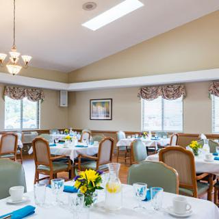 A cozy dining room setup with elegantly arranged tables, decorative flowers, and ample natural light.