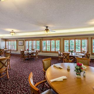 A spacious dining room with neatly arranged tables and chairs, featuring large windows and warm lighting.