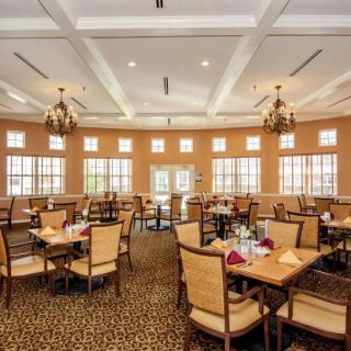 An elegant dining room with neatly arranged tables and chairs, illuminated by chandeliers.