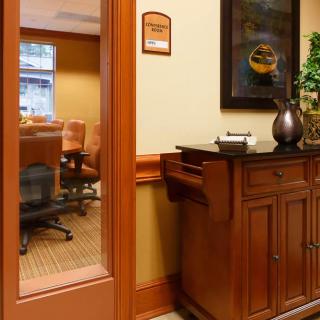 A view of a meeting room through a glass door, featuring a conference table and chairs, with a wooden cabinet in the foreground.
