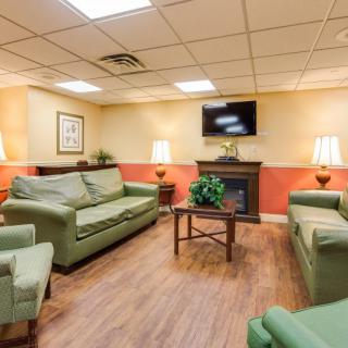 A cozy living room with green sofas, armchairs, a television mounted above a fireplace, and warm lighting.