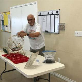 An elderly man prepares for a game of bingo, ready to draw numbers from the spinning cage.