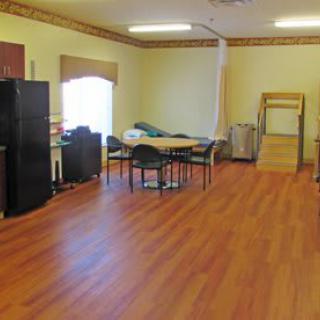 A spacious room with wooden flooring, featuring a table and chairs in the center.