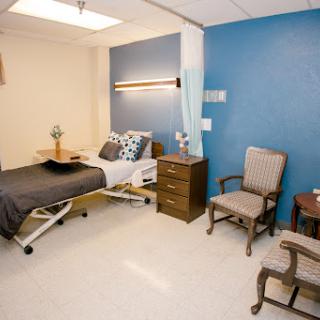 A well-furnished hospital patient room featuring a bed, chairs, and a calming blue wall.