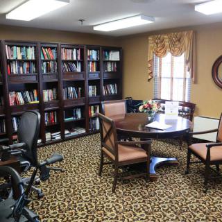 A cozy office library with bookshelves, a round table, and chairs.