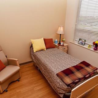A cozy bedroom with a single bed, chair, and table lamp by the window.