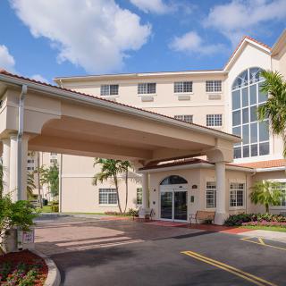A modern hotel entrance with palm trees and a covered driveway under a partly cloudy sky.