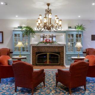 A cozy living room featuring a central fireplace, surrounded by armchairs and decorative blue cabinets, illuminated by an elegant chandelier.
