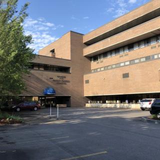 A large brick hospital building with a parking lot in front and trees surrounding it.