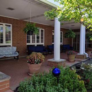 A porch with benches, potted plants, and hanging greenery under a covered area.
