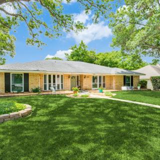 A charming suburban house with a well-maintained lawn and surrounding trees on a sunny day.