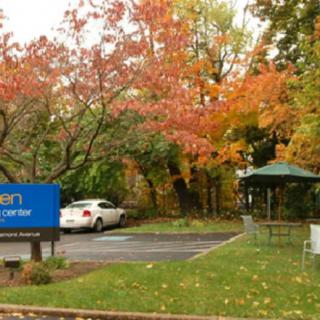 A parking lot surrounded by colorful autumn trees with a visible sign and a parked car.