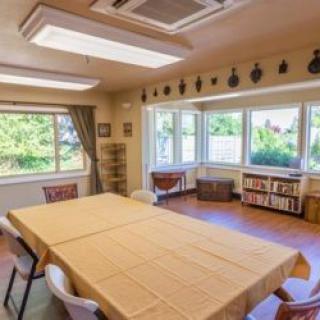 A well-lit meeting room with a large conference table, surrounded by windows and decorated with shelves and wall decor.