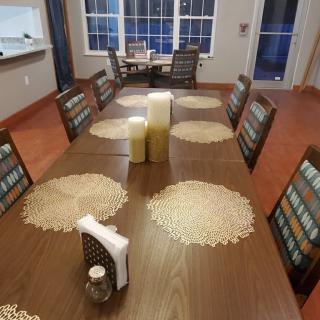 A dining room with a long table set for eight, featuring candles and circular placemats.