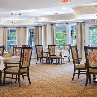 A spacious dining room with neatly arranged tables and chairs, featuring large windows and elegant curtains.
