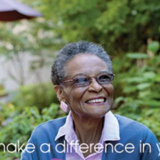 An elderly woman smiling in a garden setting.