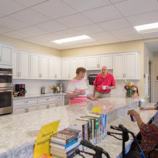 People talking in a kitchen with books on the countertop.
